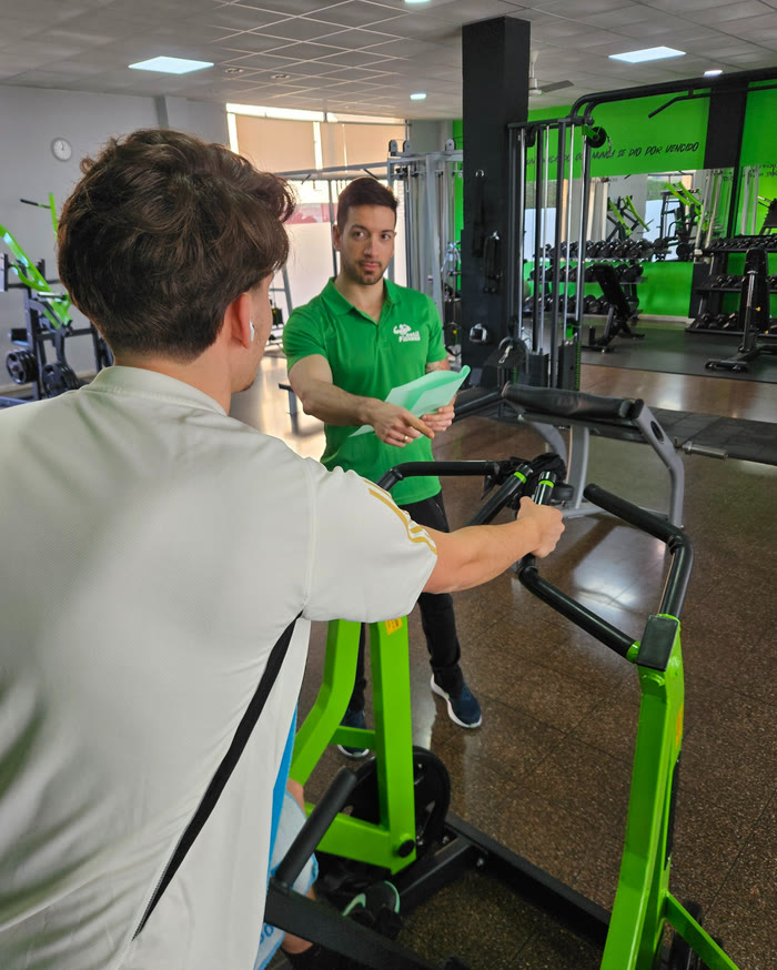 Un instructor de EstilFitness explica a un socio cómo usar una máquina