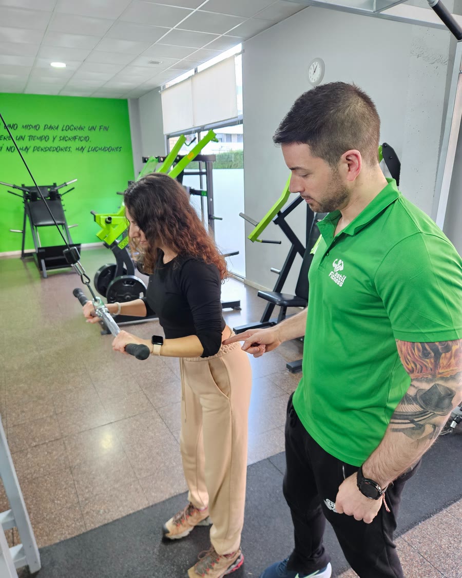 Un instructor de EstilFitness atiende a una socia mientras entrena en la polea